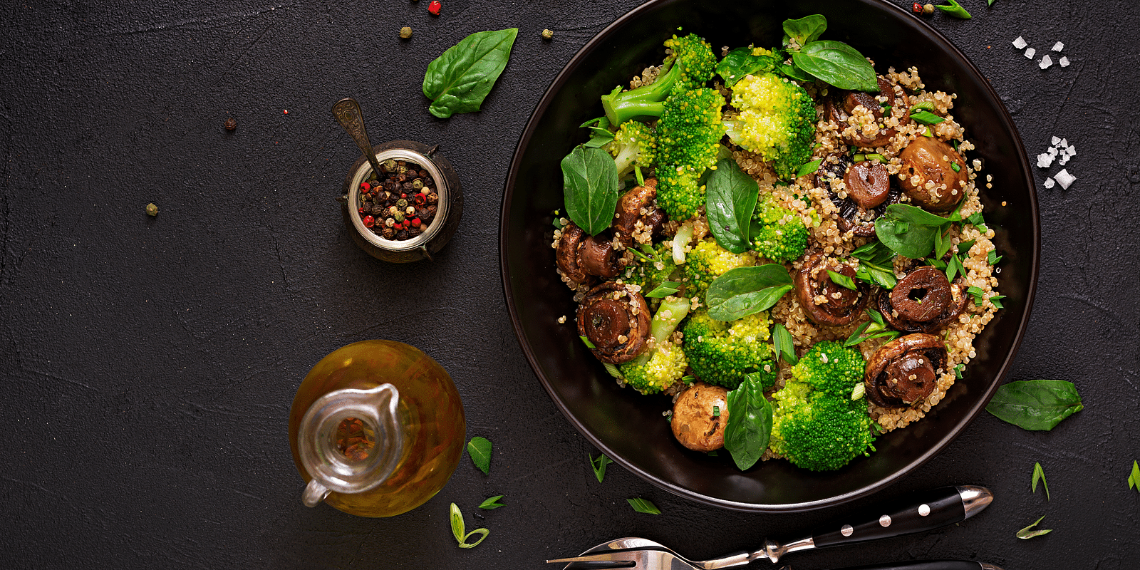 a pan with quinoa, mushrooms and broccoli with a container of peppercorns beside it